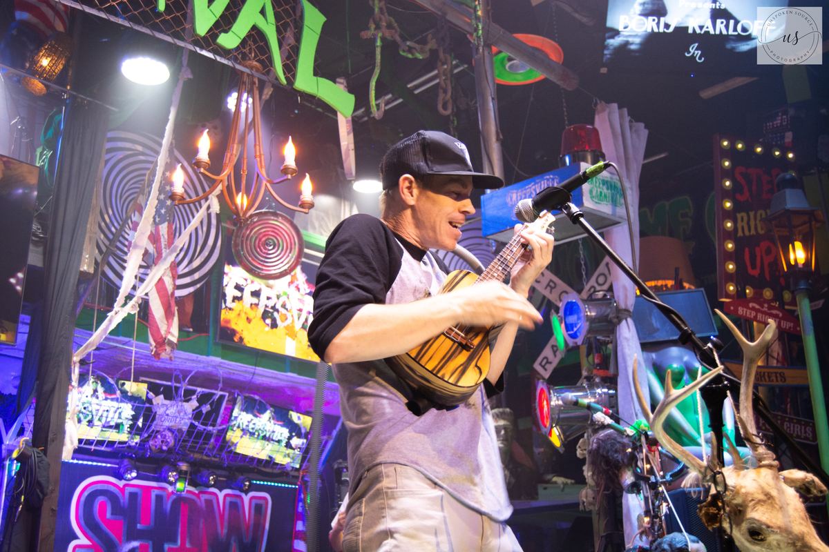 Ryan performing on stage with a ukulele at a carnival-themed venue